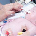 Portrait of newborn baby and hand inside incubator